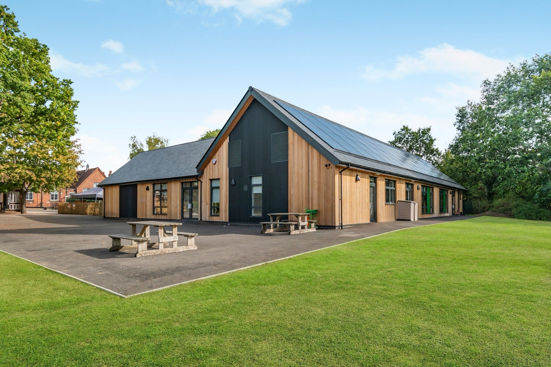 A single-storey timber-clad building whose tall gable end is clad in dark vertical slats