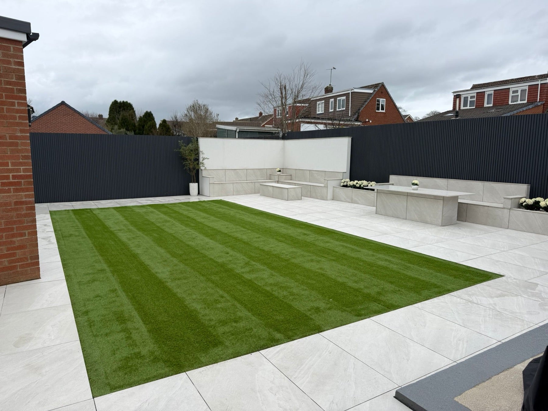 Dark vertical slatted walls round a garden with a porcelain patio, built-in benches and artificial grass